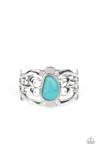 An asymmetrical turquoise stone is pressed into the center of a silver cuff layered with filigree patterns around the wrist for a rustic flair.