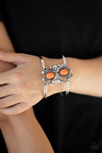Load image into Gallery viewer, A leafy silver flower blooms between two oval orange stones atop a studded and filigree filled backdrop, creating a subtly slanted centerpiece across the airy silver cuff.
