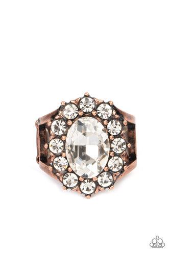 Paparazzi - Moxie Magic - Copper -  A dauntless oval rhinestone is encircled by dainty sparkling gems. Accented with petite antiqued copper studs, the dramatic design joins with an airy layered copper band to create a captivating arrangement atop the finger.